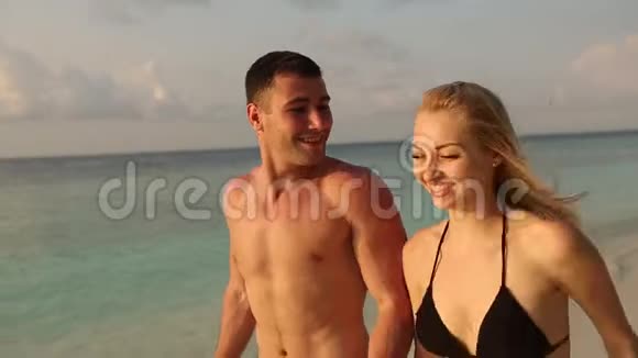一对年轻夫妇手牵着手在海滩上冲浪新婚夫妇度蜜月享受假期恋人泼蓝色视频的预览图