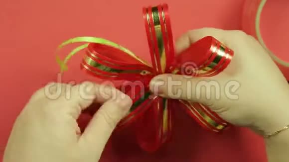 女人的手拉直了粉红丝带礼物蝴蝶结的花瓣并把它做成蝴蝶结的形状红色背景视频的预览图