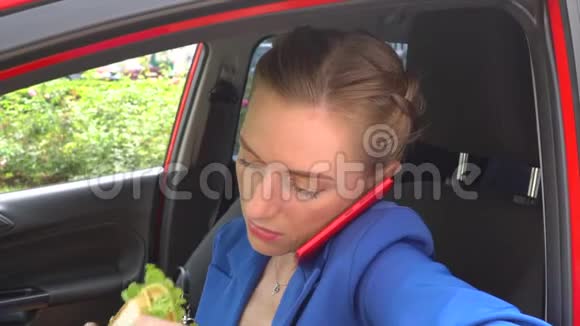 女人坐在车里吃午饭她咬三明治喝杯咖啡女孩很忙她在说话视频的预览图