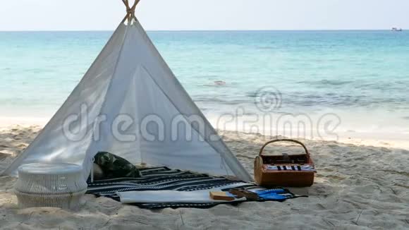 4K浪漫的白色野餐帐篷白色沙滩上有篮子食物背景是清澈的水和蓝天视频的预览图