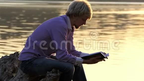 学生坐在湖畔读一本手册视频的预览图