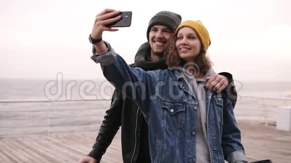快乐的年轻夫妇在阴天附近用手机自拍戴着黄色帽子的女孩视频的预览图