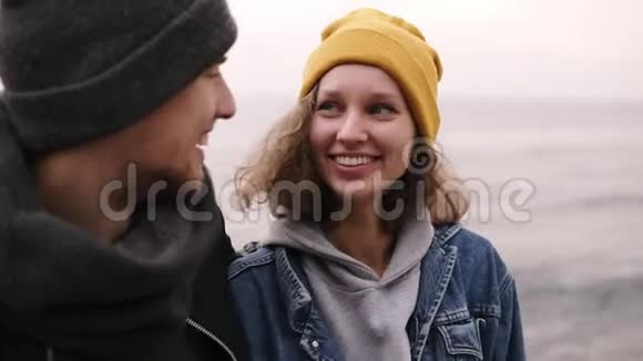 一对时髦的年轻幸福夫妇站在一起在海边拥抱穿暖和衣服的年轻人视频的预览图