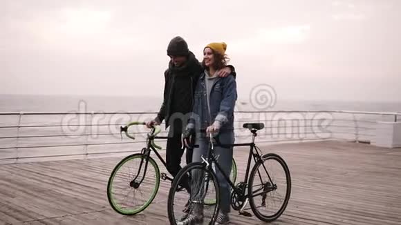 美丽的微笑的一对年轻的嬉皮士在秋日和他们的自行车一起拥抱在海边青年视频的预览图