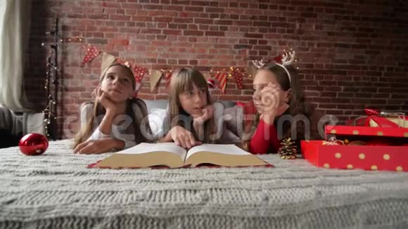 三姐妹穿着柔软的睡衣躺在床上三胞胎读着一本巨大的圣诞故事书卧室装饰着视频的预览图