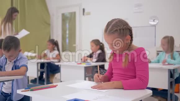 小女生在灯光教室里画画的肖像坐在同学和年轻的背景下的课桌后面视频的预览图