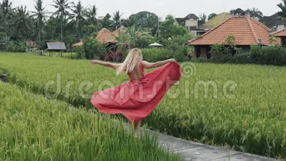 一个欧洲女孩在巴厘岛村庄的稻田里享受着孤独她在露台上旋转手里拿着她的裙子视频的预览图