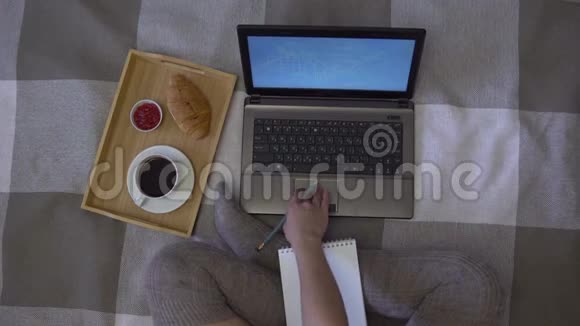 头顶上的镜头女孩在笔记本电脑旁边的床上画了一张记事本还有一杯咖啡和一个羊角面包视频的预览图