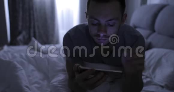 晚上睡觉前带着智能手机躺在床上的男人视频的预览图