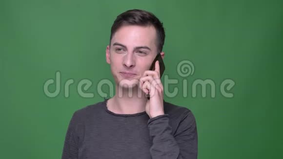 年轻英俊的白种人男性特写镜头在绿色背景下与电话交谈视频的预览图