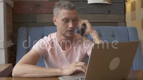英俊的商人在电话里说话在笔记本电脑上工作时微笑视频的预览图