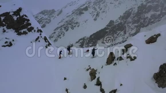 雪灾期间三名滑雪者站在一座山峰上的美丽空中镜头4k视频的预览图