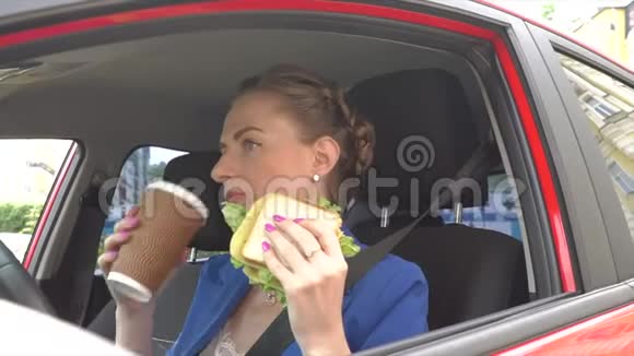 不开心的女人坐在车里吃午饭她吃三明治喝咖啡女孩也用汽车喇叭她在交通方面视频的预览图