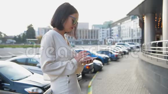 在一个阳光明媚的日子里穿着白色衬衫的女人在街上走着用智能手机发短信视频的预览图