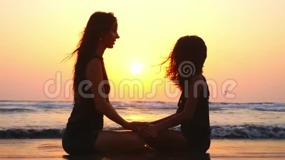 日落时分妈妈和女儿一起坐在沙滩上手牵手视频的预览图