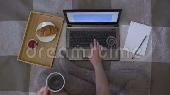头顶射中女孩在手里拿着一杯咖啡在笔记本电脑上打字她旁边有一个笔记本和一个视频的预览图
