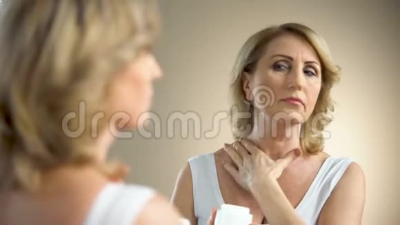 老年妇女在颈部和颈部涂抹滋养霜抗老年护理视频的预览图