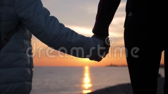 母亲和女儿在海滩上散步的剪影手握日落背景快关门视频的预览图