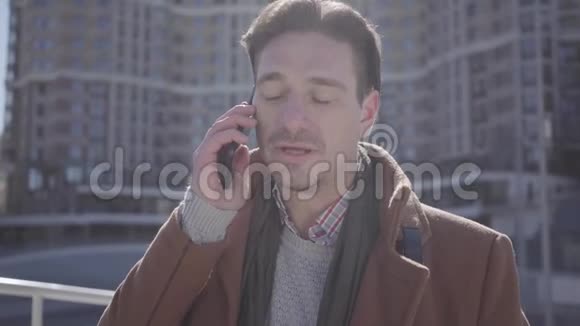 身着棕色外套的英俊自信男子站在城市街道上用手机交谈的肖像城市景观视频的预览图