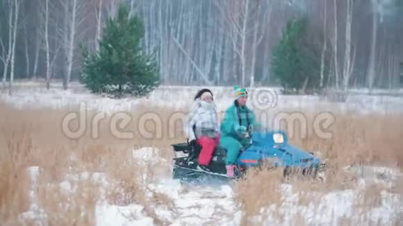 在冬天的森林里在冰冻的草地上骑着雪地摩托的年轻人视频的预览图