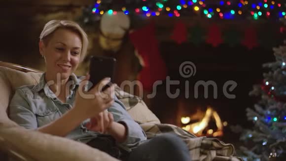 在圣诞夜壁炉前使用智能手机聊天的成年美女视频的预览图