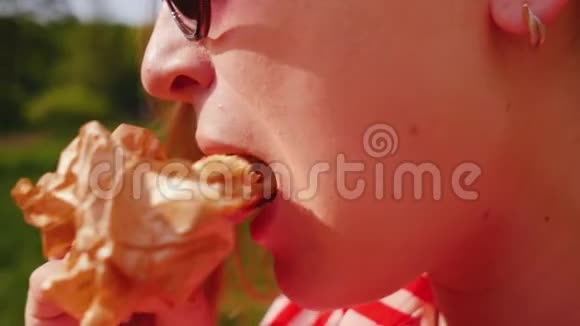 女孩拿着三明治在露天吃新鲜的糕点近距离射击视频的预览图