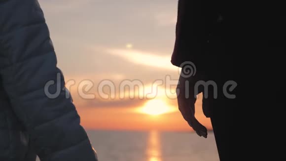 母亲和女儿在海滩上散步的剪影手握日落背景快关门视频的预览图