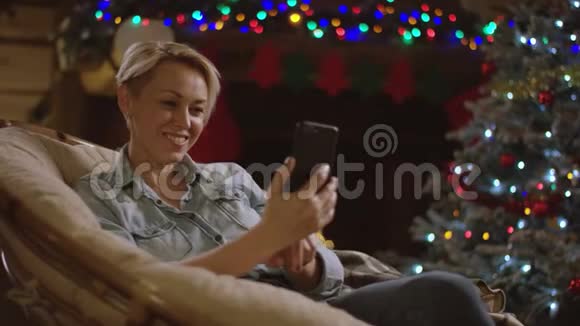 在壁炉前的圣诞夜美丽的女人用手机交流视频的预览图