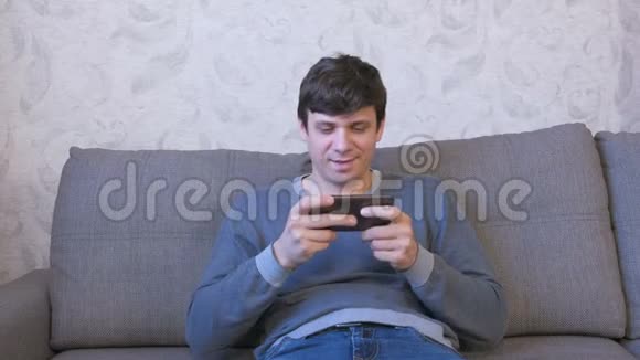 男人坐在沙发上用手机玩游戏视频的预览图