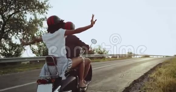 骑摩托车的女孩正挥手向空中挥手因为她和她一起去长途旅行感到兴奋视频的预览图