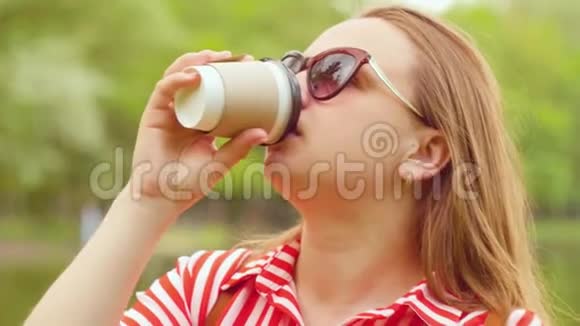 夏天女孩站在公园里喝塑料杯里的咖啡近距离射击视频的预览图