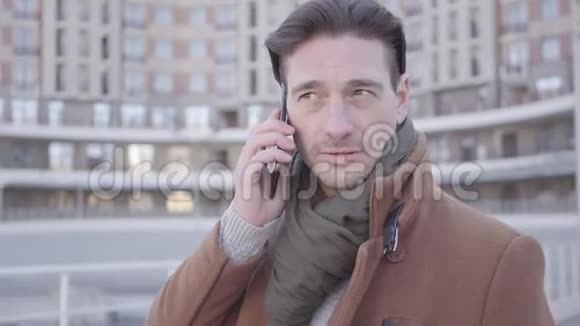 身着棕色外套的英俊自信男子站在城市街道上用手机交谈的肖像城市景观视频的预览图