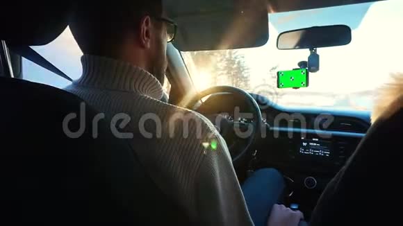 冬天在阳光明媚的公路上开车的人智能手机的挡风玻璃上有一个绿色的屏幕一个男人视频的预览图