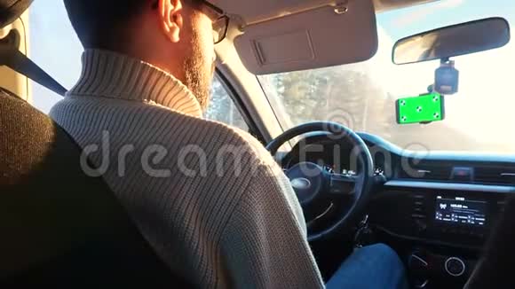 冬天在阳光明媚的公路上开车的人智能手机有一个绿色屏幕连接在挡风玻璃上视频的预览图