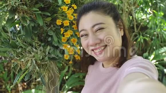 快乐的亚洲女人在花园里和美丽的兰花合影视频的预览图