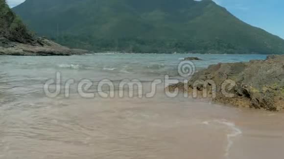 海水在热带岛屿的岩石海滩上飞溅石岸上美丽的海浪森林覆盖的山地视频的预览图