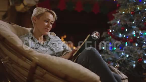 成年金发女人在圣诞节晚上读一本书视频的预览图