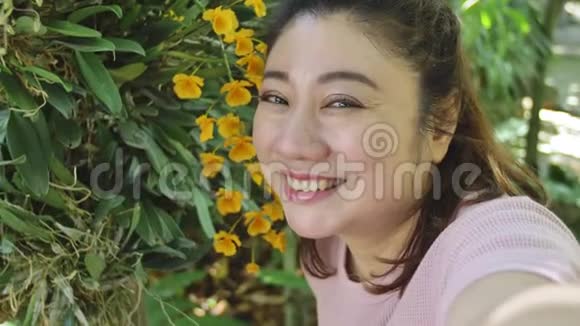 快乐的亚洲女人在花园里和美丽的兰花合影视频的预览图
