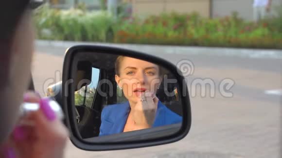 迷人的女孩坐在车里用口红她为嘴唇化妆女孩照镜子视频的预览图
