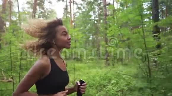 年轻美丽的非洲裔美国妇女卷发在森林里伴着音乐奔跑亲密无间视频的预览图