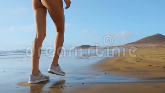 紧身的腿部运动女性穿着白色运动鞋在美丽的沙滩上奔跑健康的生活方式慢视频的预览图