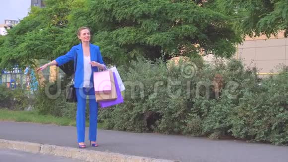 幸福的女人站着拿着购物袋她微笑着女孩用手挥手在那辆车停下来之后她坐着视频的预览图