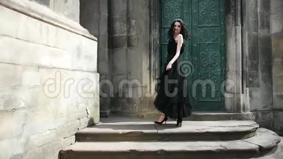 女孩黑发穿着黑色长裙戴着皇冠摆姿势靠近老建筑视频的预览图