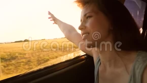 快乐女孩坐在车里把手从窗户里拉出来笑在炎热的夏天他从车窗里挥手视频的预览图