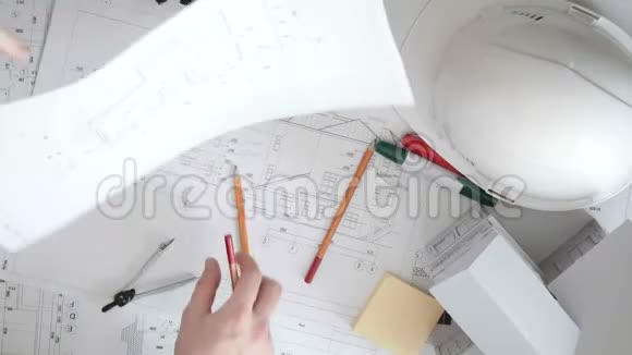 在一张放铅笔记号笔和头盔的大桌子上用手整理建筑的大图视频的预览图
