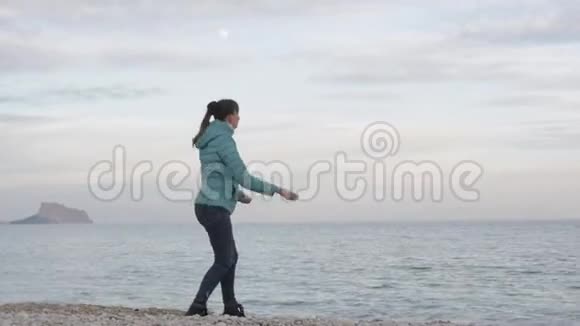 孤独寒冷海滩的女人白种人女人在山上和满月的背景下把石头扔进平静的大海视频的预览图