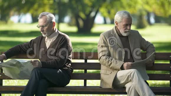 两个被冒犯的老人看报纸坐在公园的长凳上吵架视频的预览图