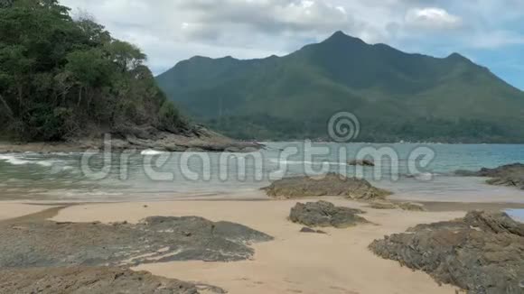 海水在热带岛屿的岩石海滩上飞溅石岸上美丽的海浪森林覆盖的山地视频的预览图