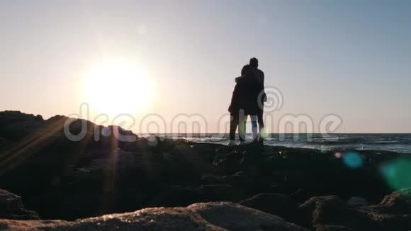 男朋友和女朋友的剪影站在海滩边看着地平线年轻的幸福夫妇站在海边拥抱视频的预览图