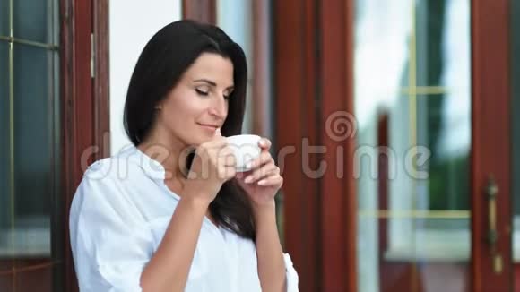 手捧着白瓷杯喝热茶或咖啡的英俊黑发女人视频的预览图